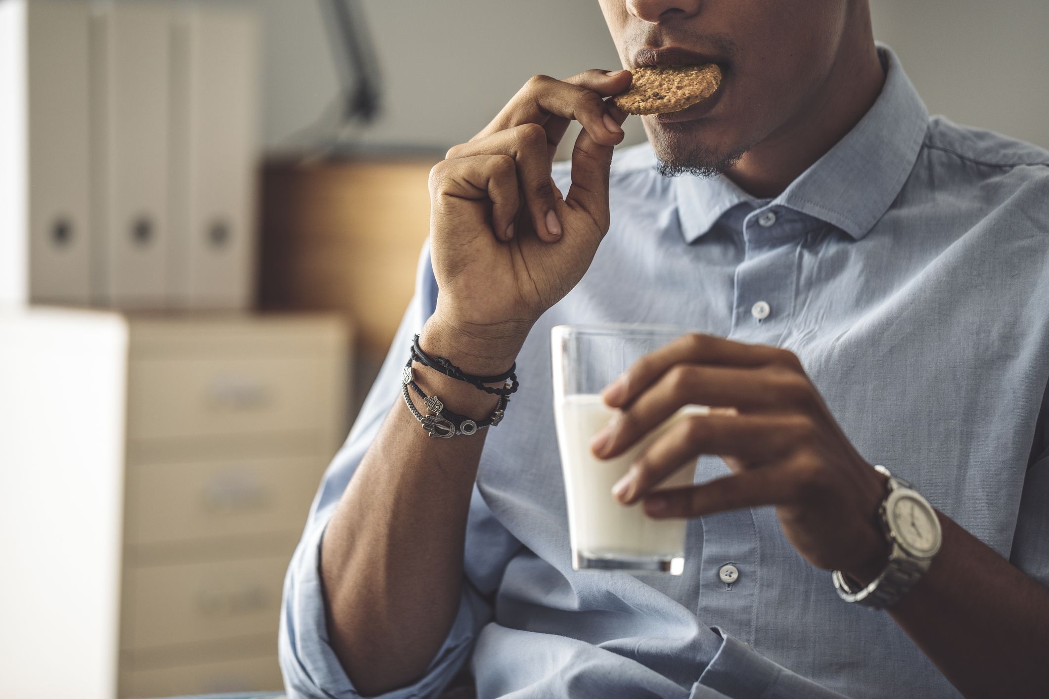 A man is eating a cookie and holding a glass of milk in his left hand