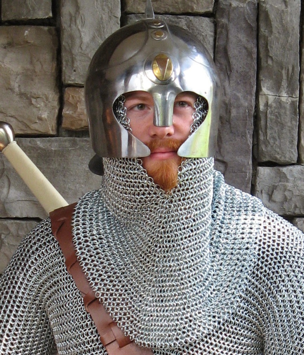 A man wearing a chain mail armor suit, armor helmet, and a brown leather belt