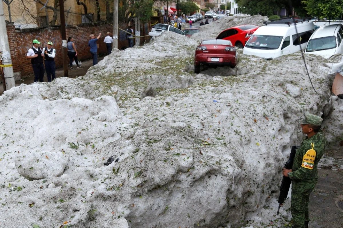 People standing next to a road completely covered by a hailstorm