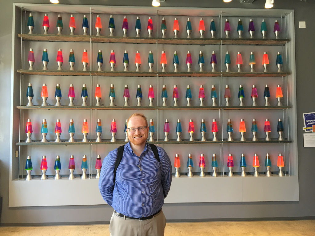 A man wearing blue shirt standing next to Cloudflare's lava lamp wall
