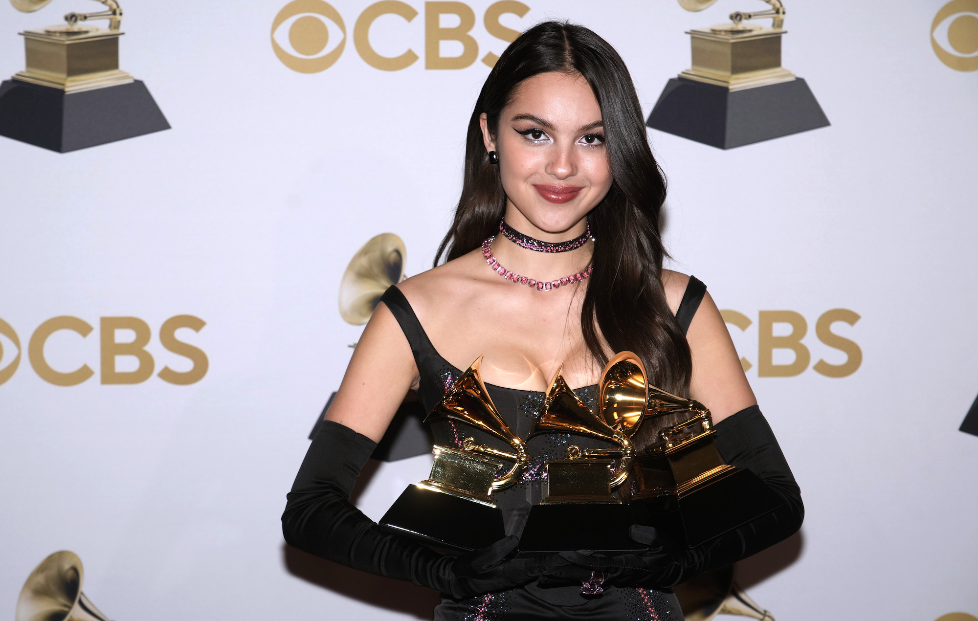 Olivia Rodrigo at Grammys 2022 winners room holding her 3 Grammy awards