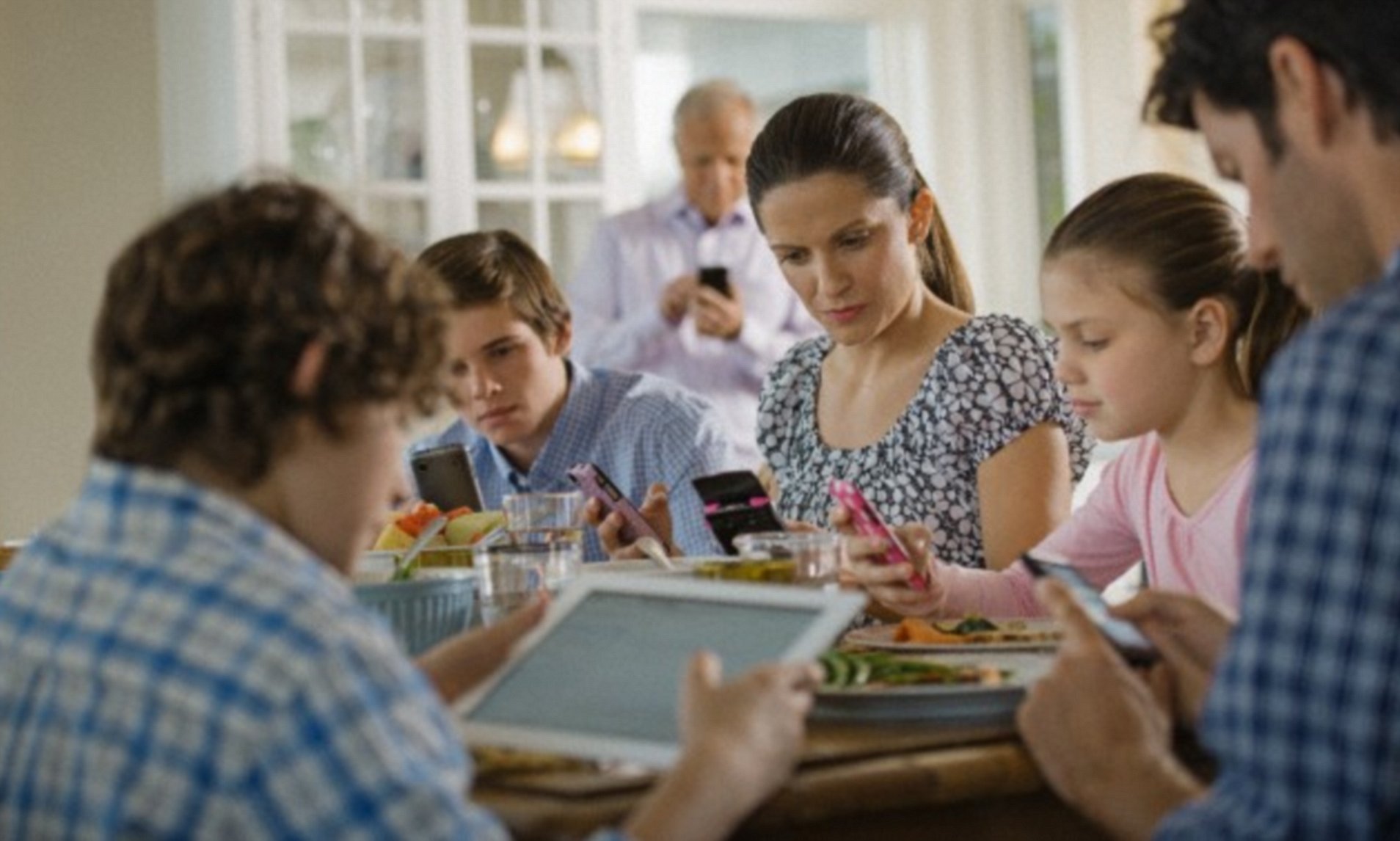 Everyone is busy with their phones and other devices during a family meal