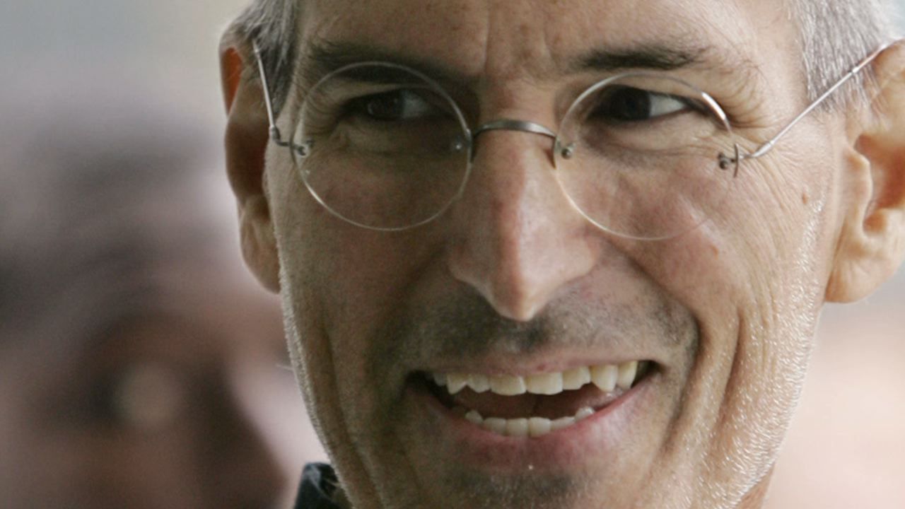 Steve Jobs wearing round-frame glasses and laughing