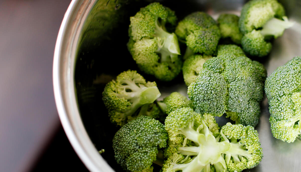 Some chunks of yellow and green foresty tops of brocolli are in the stainless steel cooking pot