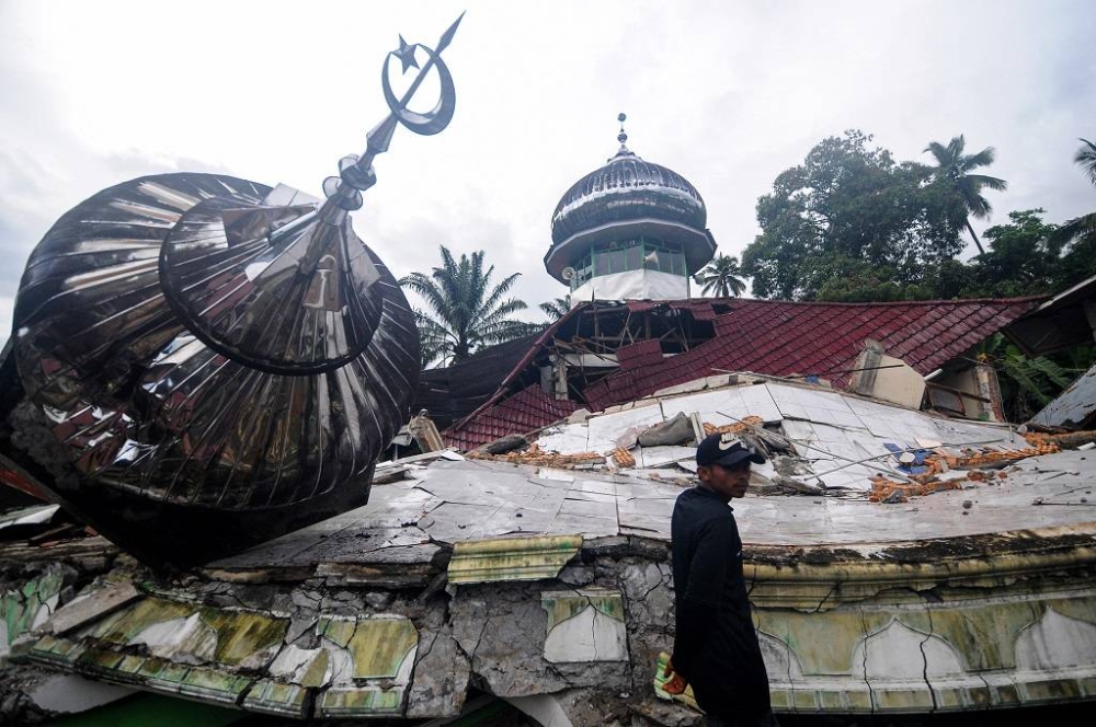 A man standing next to mosques affected by earthquake