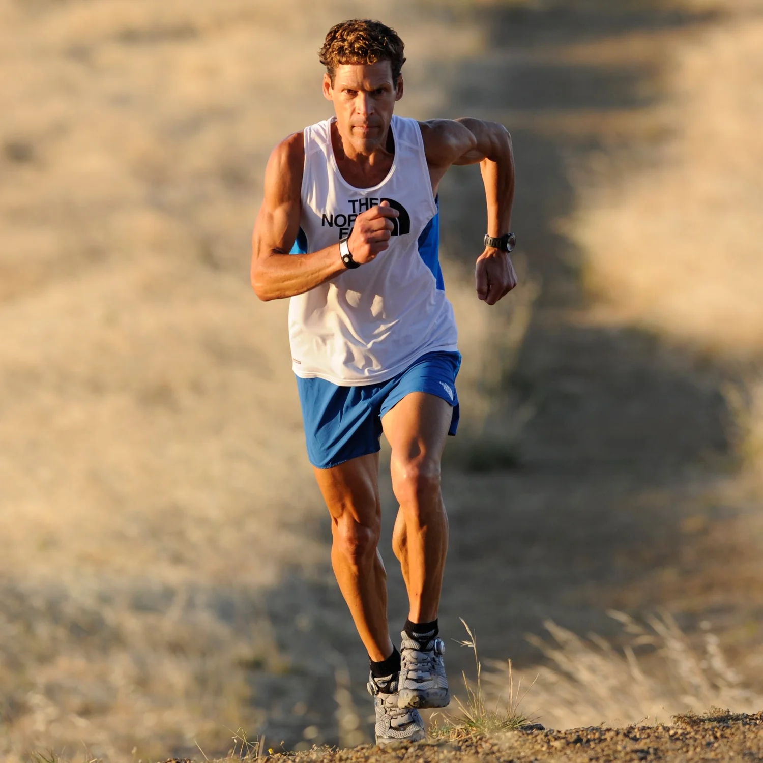 Dean Karnazes wearing white vest and blue shorts and running 