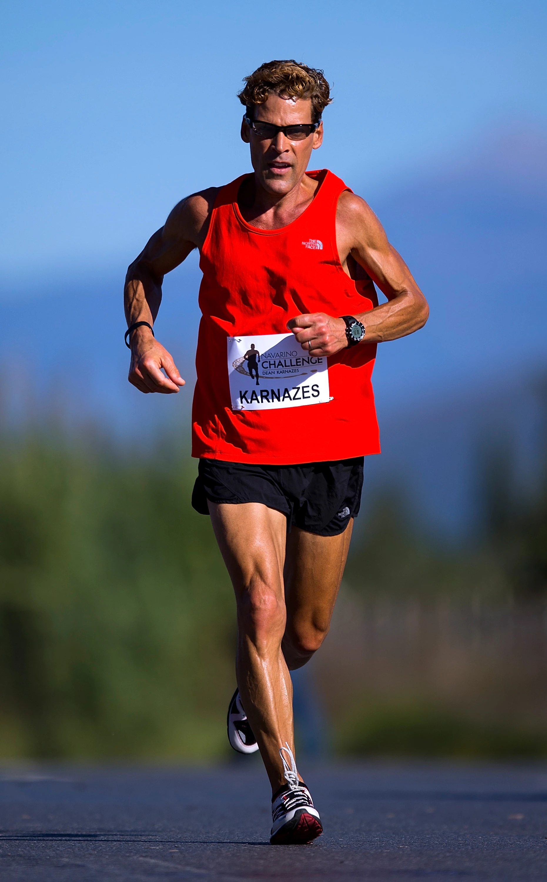 Dean Karnazes wearing red shirt and black shorts while running on road