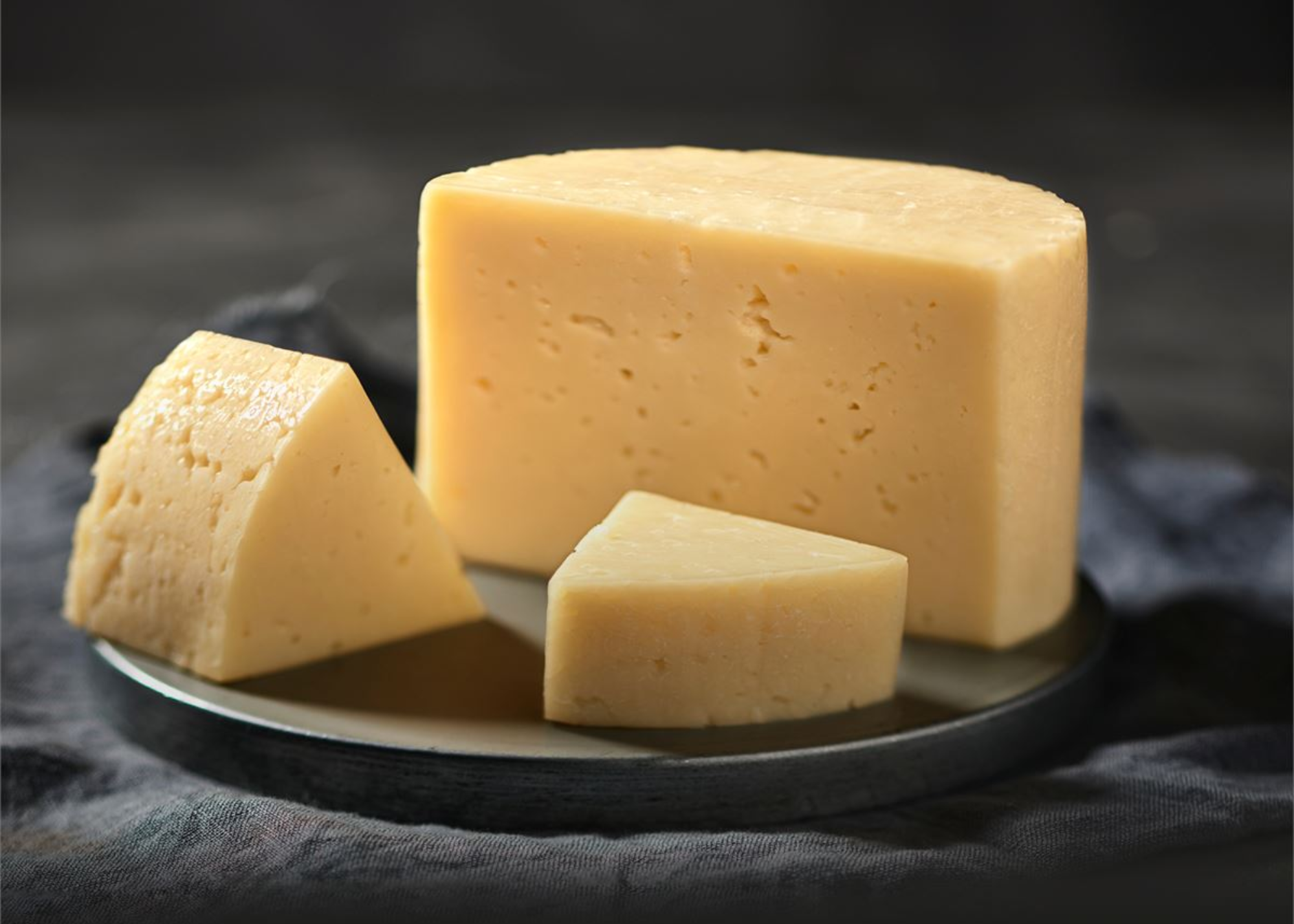 A whole Tilsit cheese is cut into small pieces, revealing numerous small holes and cracks