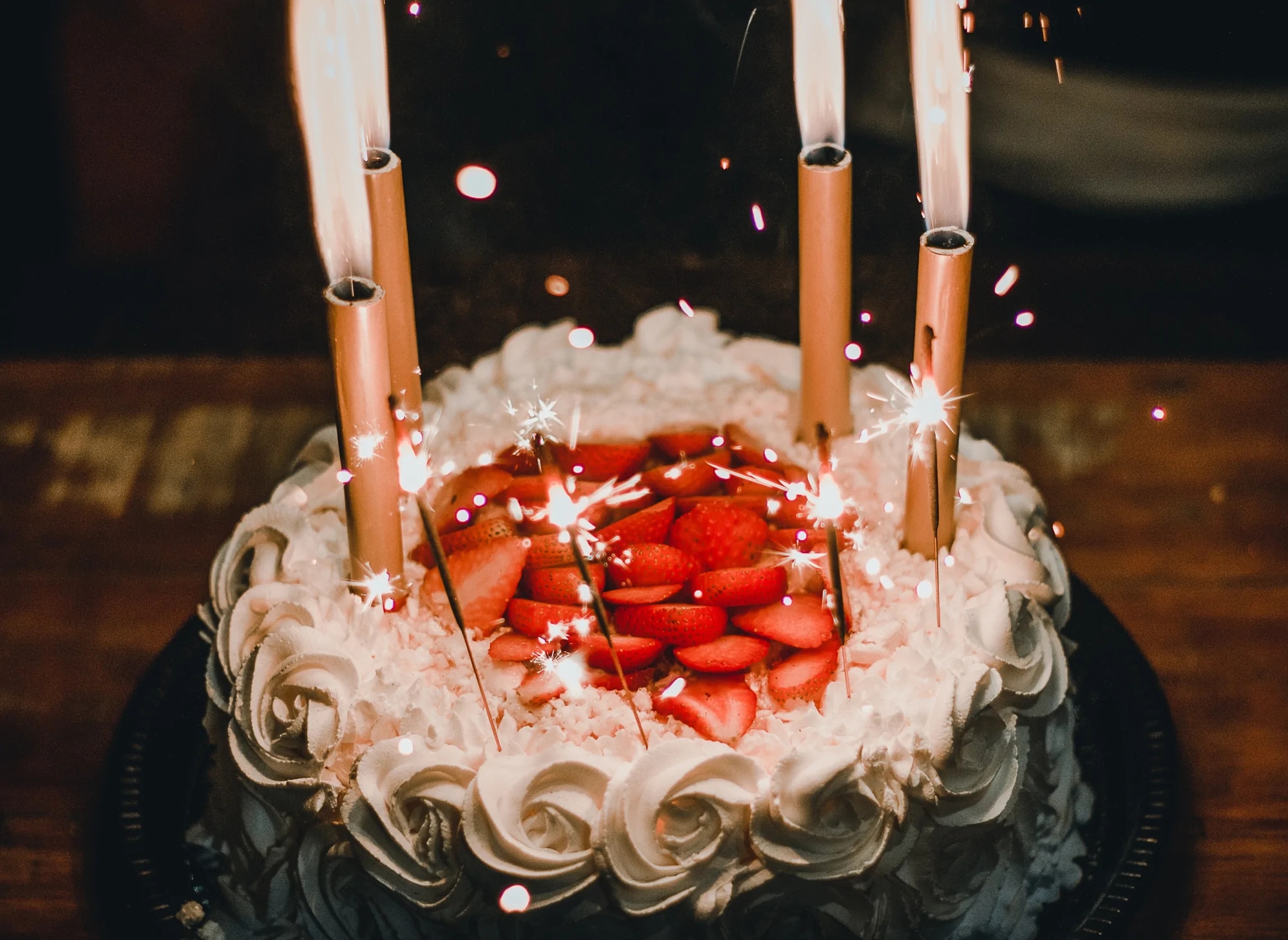 A cake with strawberry slices and white cream flowers and is decorated with candles