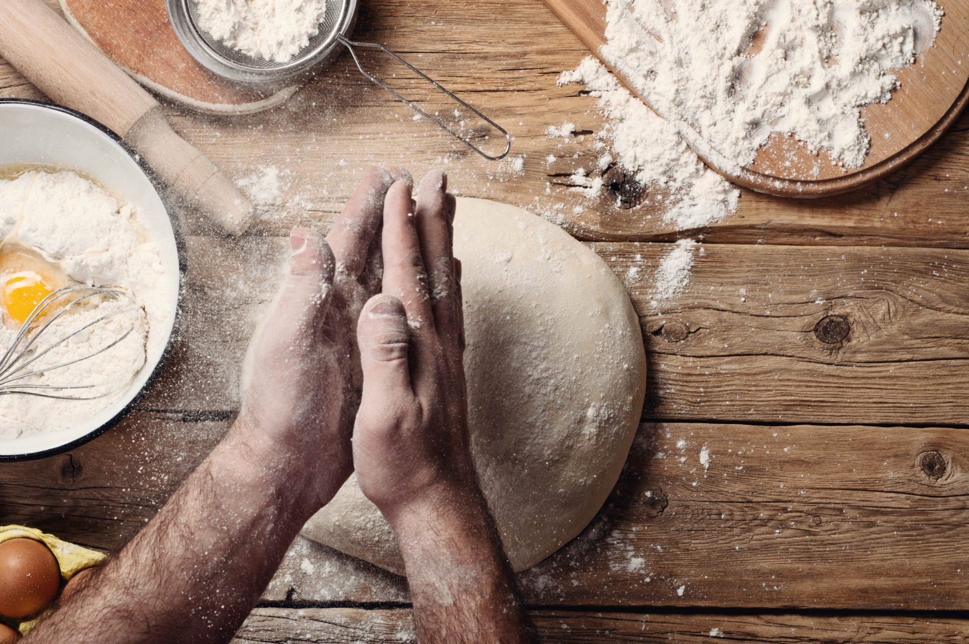 A man's hands dusting flour on a dough ball
