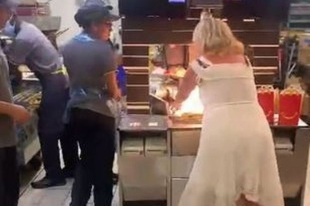 A woman in white dress standing next to a cooking counter in Mcdonald's and McD staff is in confusion seeing what that lady is doing