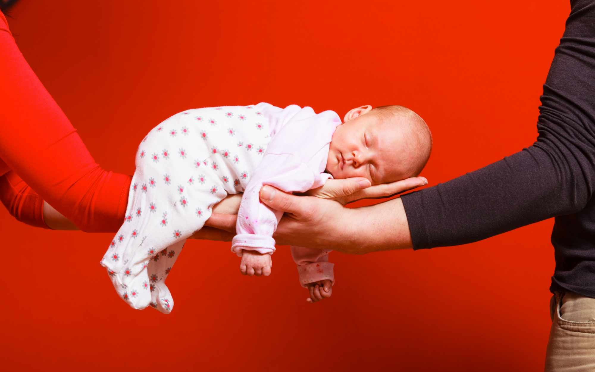 A sleeping baby rests on the hands of two people