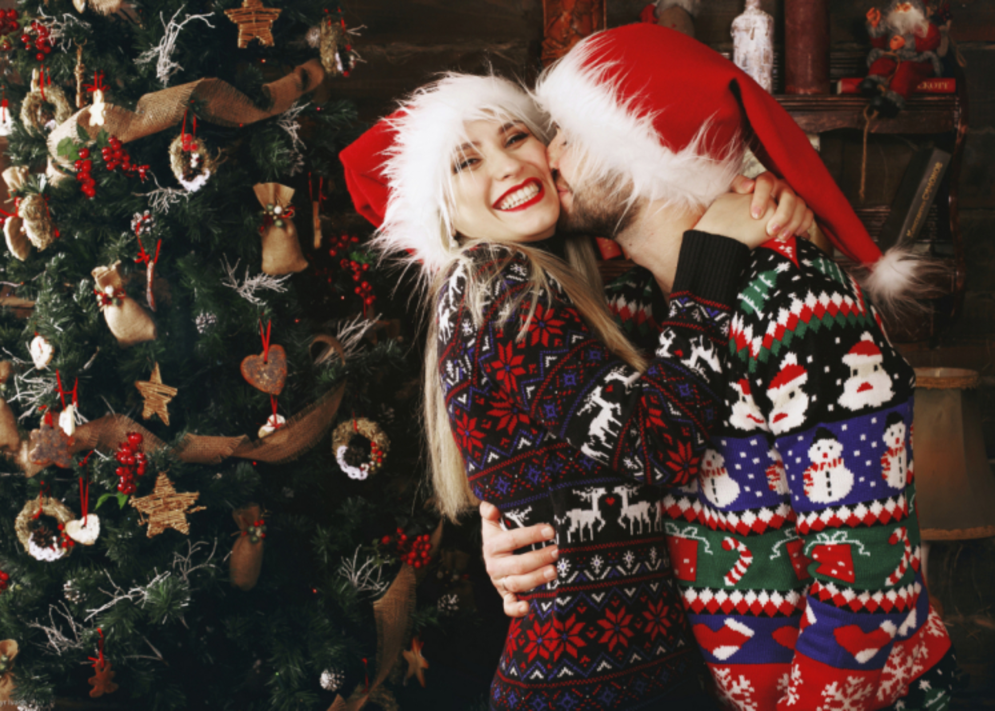 A man kissing a woman, with a Christmas tree in the background