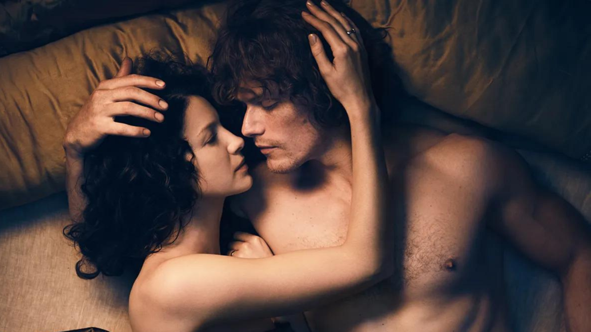 A naked man and woman looking at each other while lying in the bed