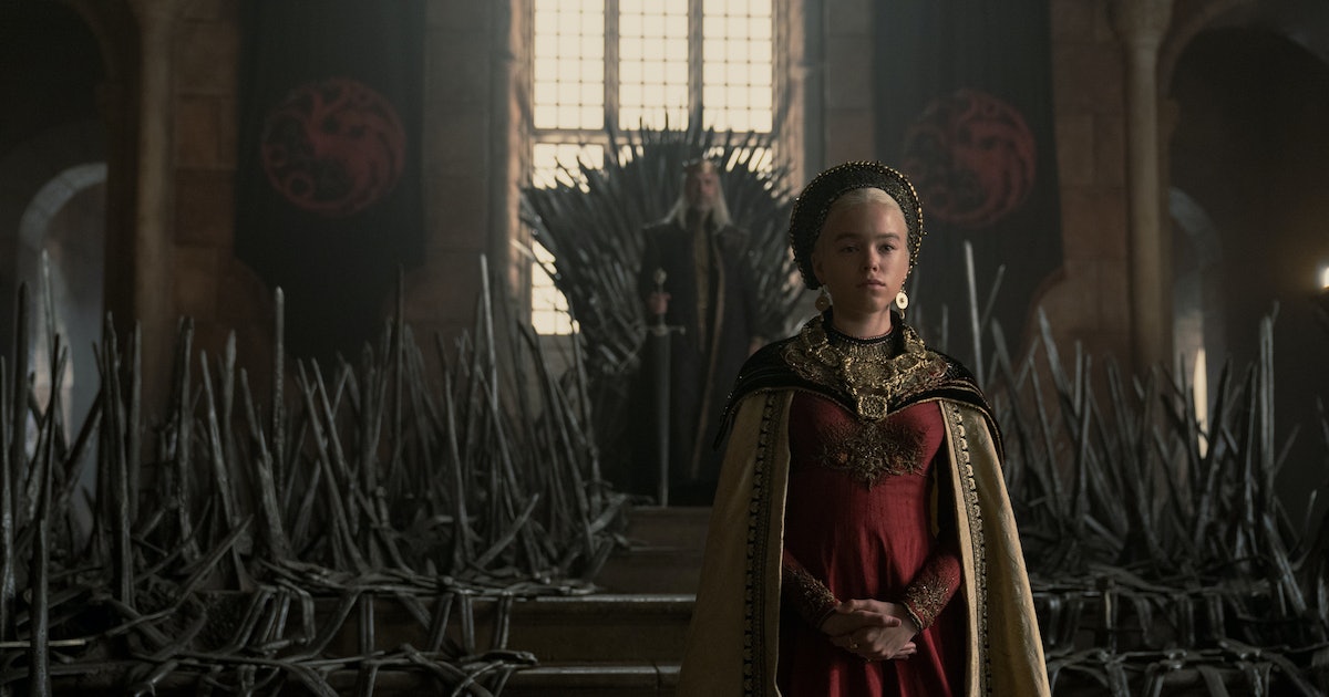 A girl wearing a maroon gown standing next to a throne