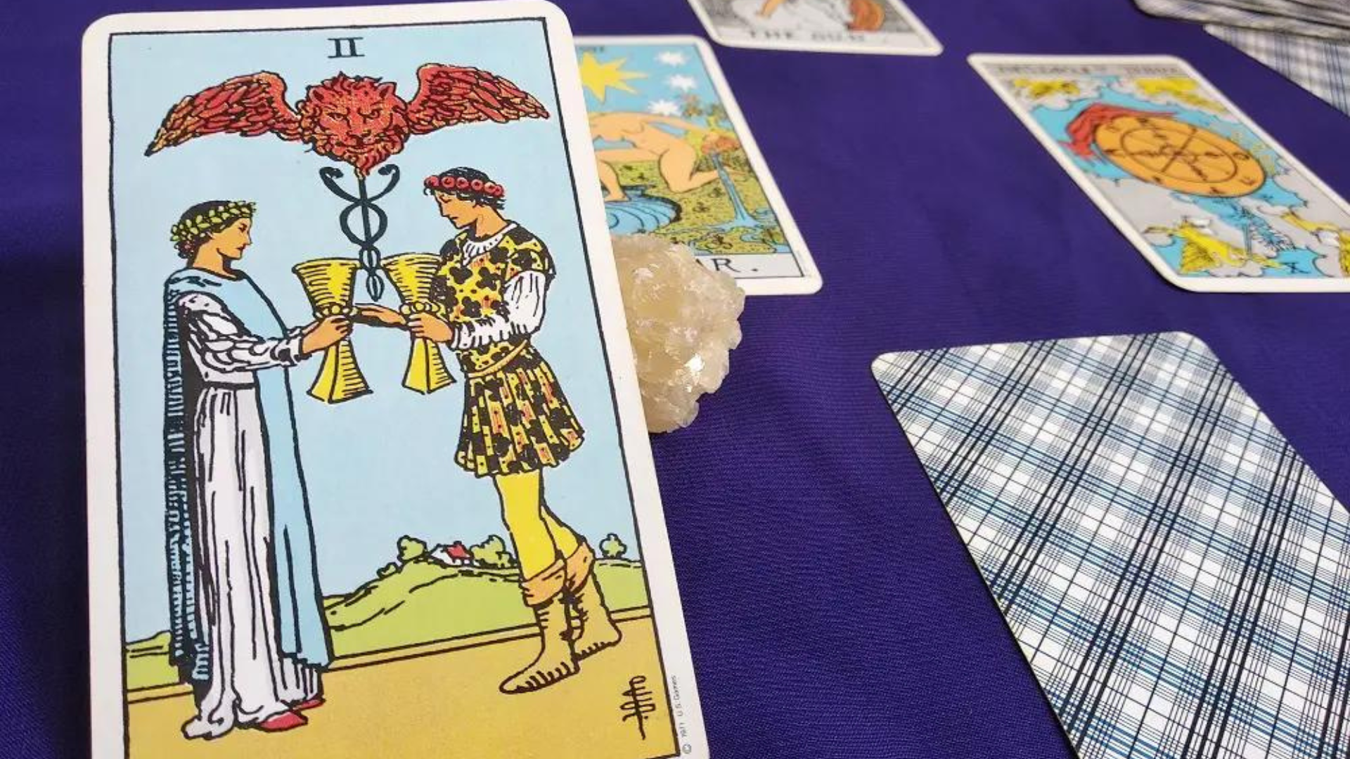 Two Of Cups Upright Card placed on a violet table along with other cards and a crystal