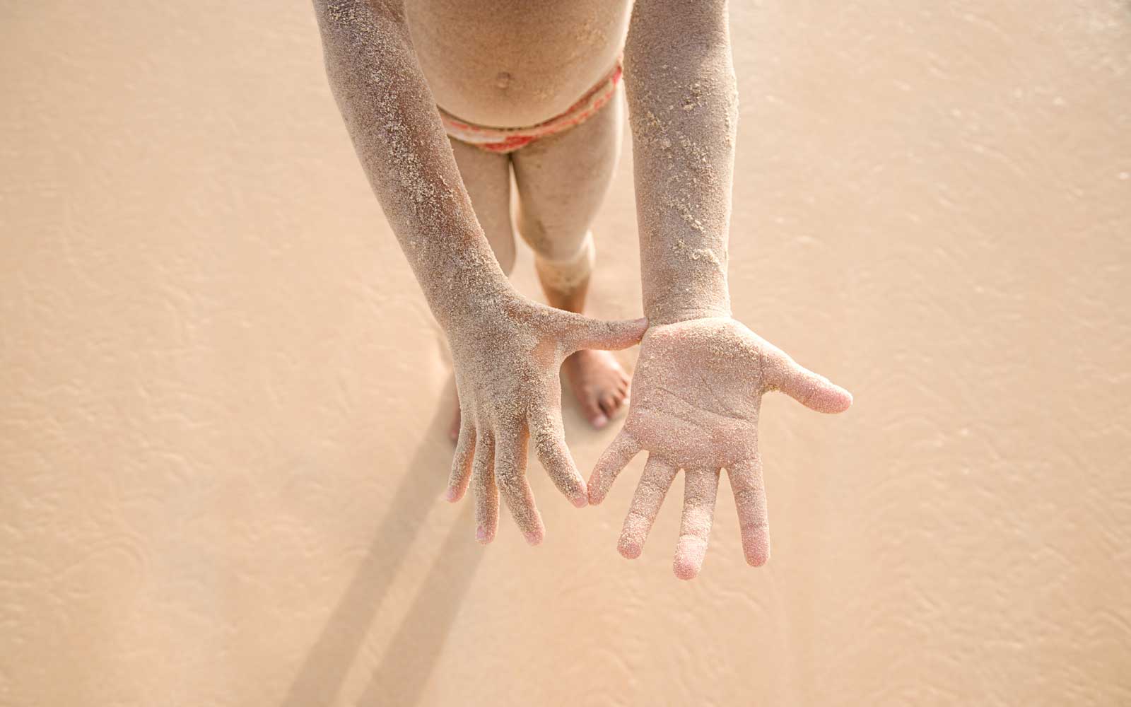 A young child showing its hands that is covered with fine sands in the beach