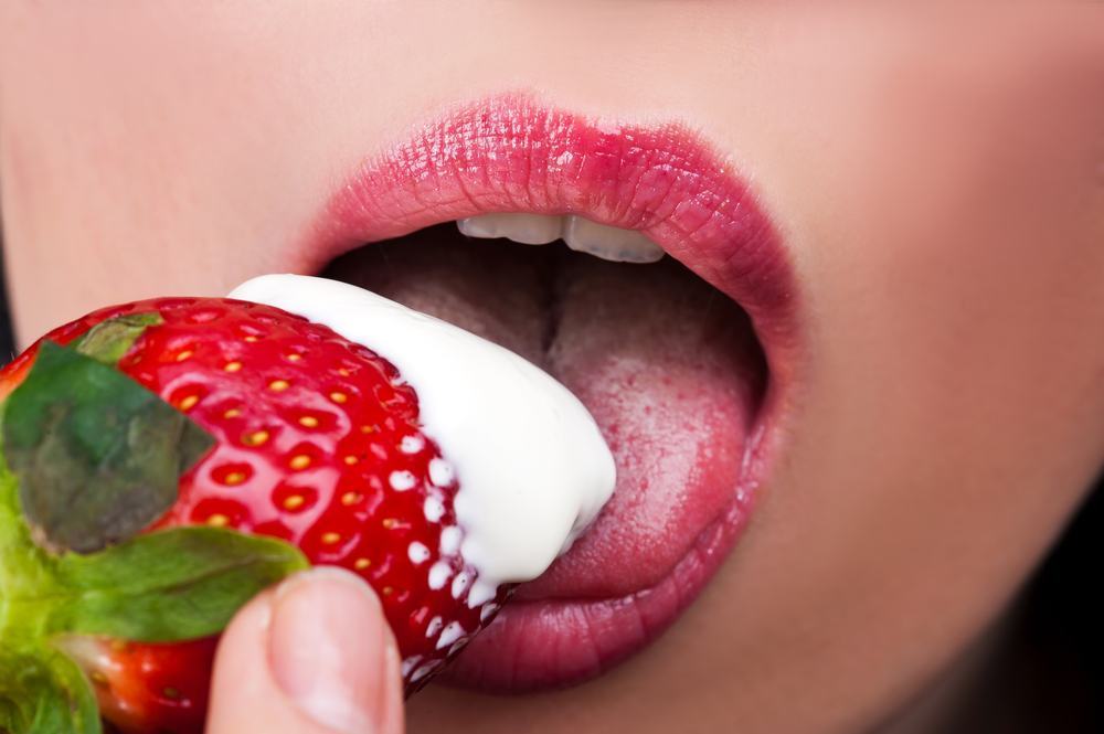 A woman eating a strawberry with cream