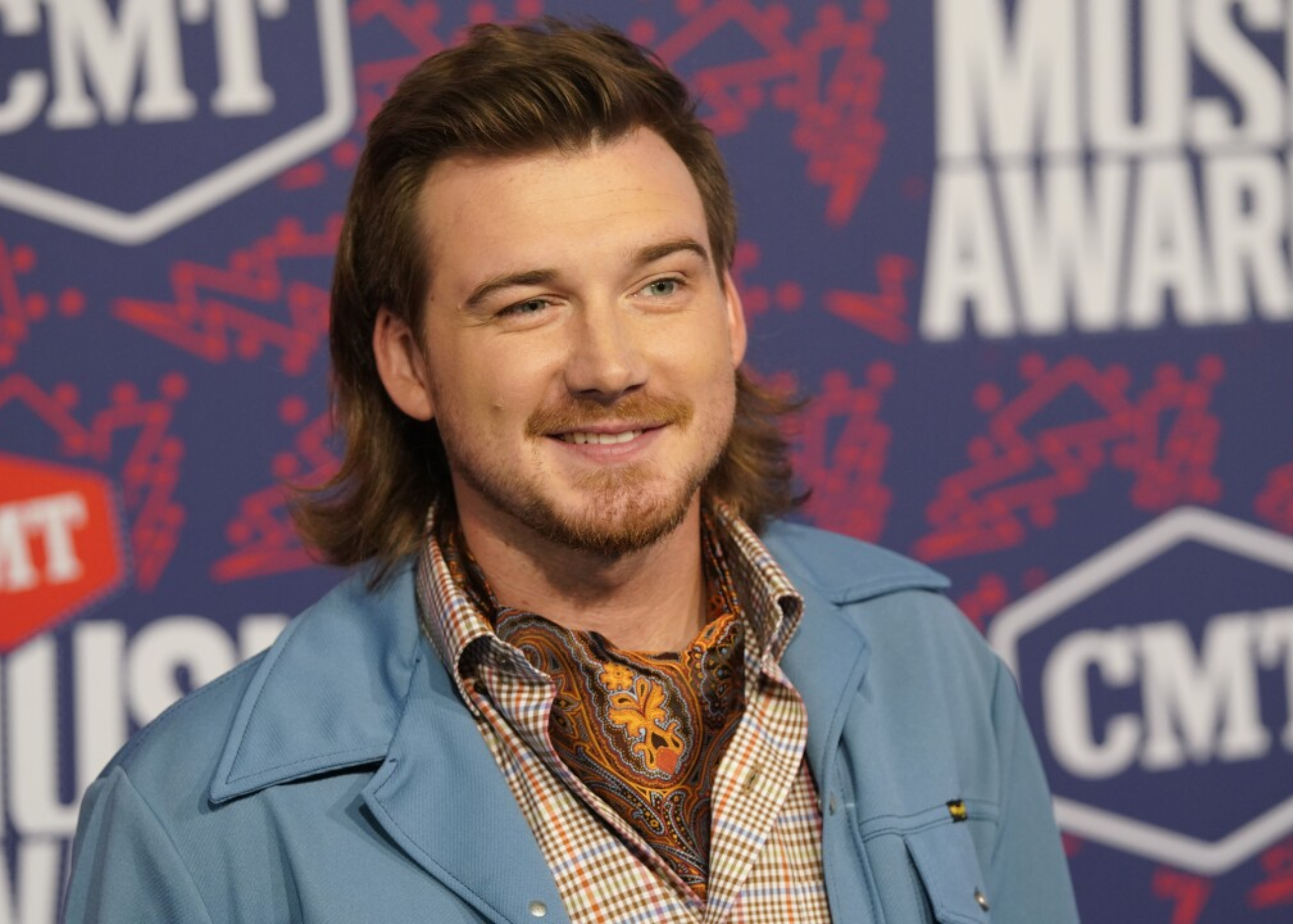 Morgan Wallen is smiling to the camera while wearing skyblue-colored coat