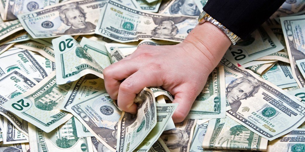 A man's hand can be seen crumpling the paper money