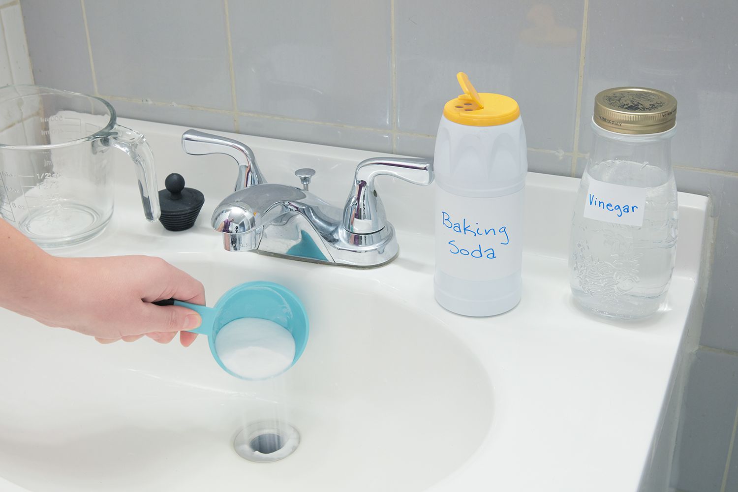 A person pouring drain cleaner in a white bathroom sink