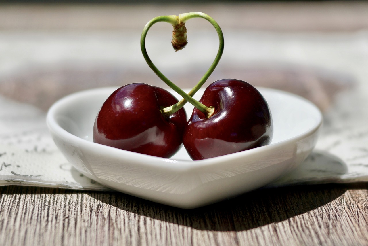 2 Cherries joined together by their small branch in a small heart-shaped plate