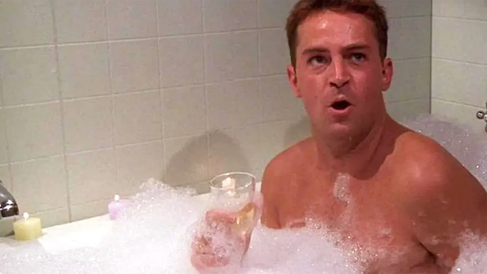 A man taking a bubble bath and having a glass of wine