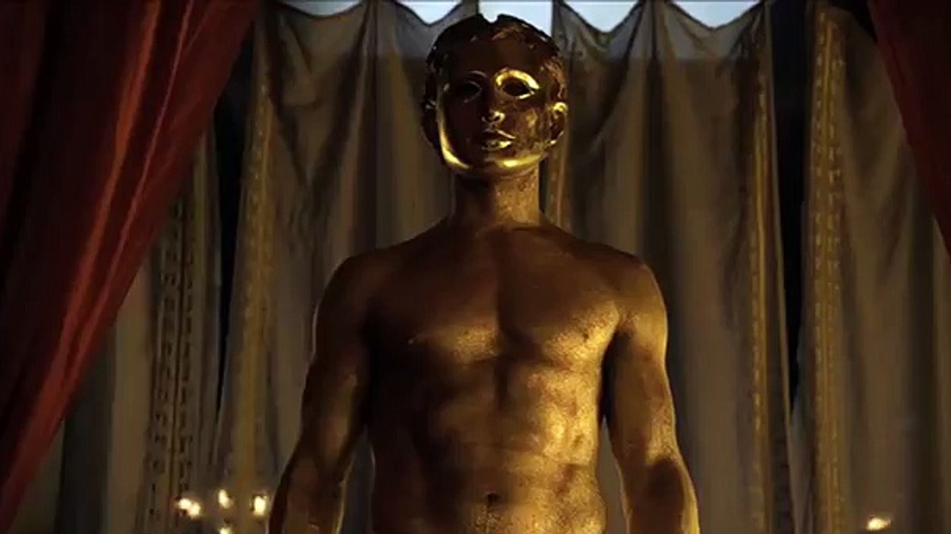 A top less man with gold glitters on skin wearing a golden mask