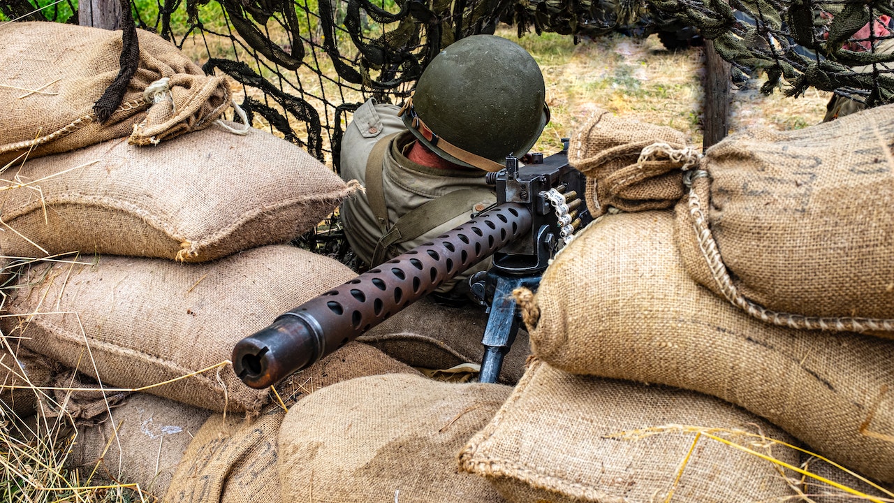 Person Wearing M1 Helmet While Holding A Machine Gn Ad Sitting On A Pile Of Sacks