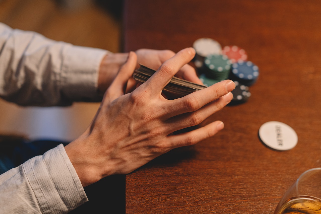 A Person Holding a Playing Cards Near the Wooden Table