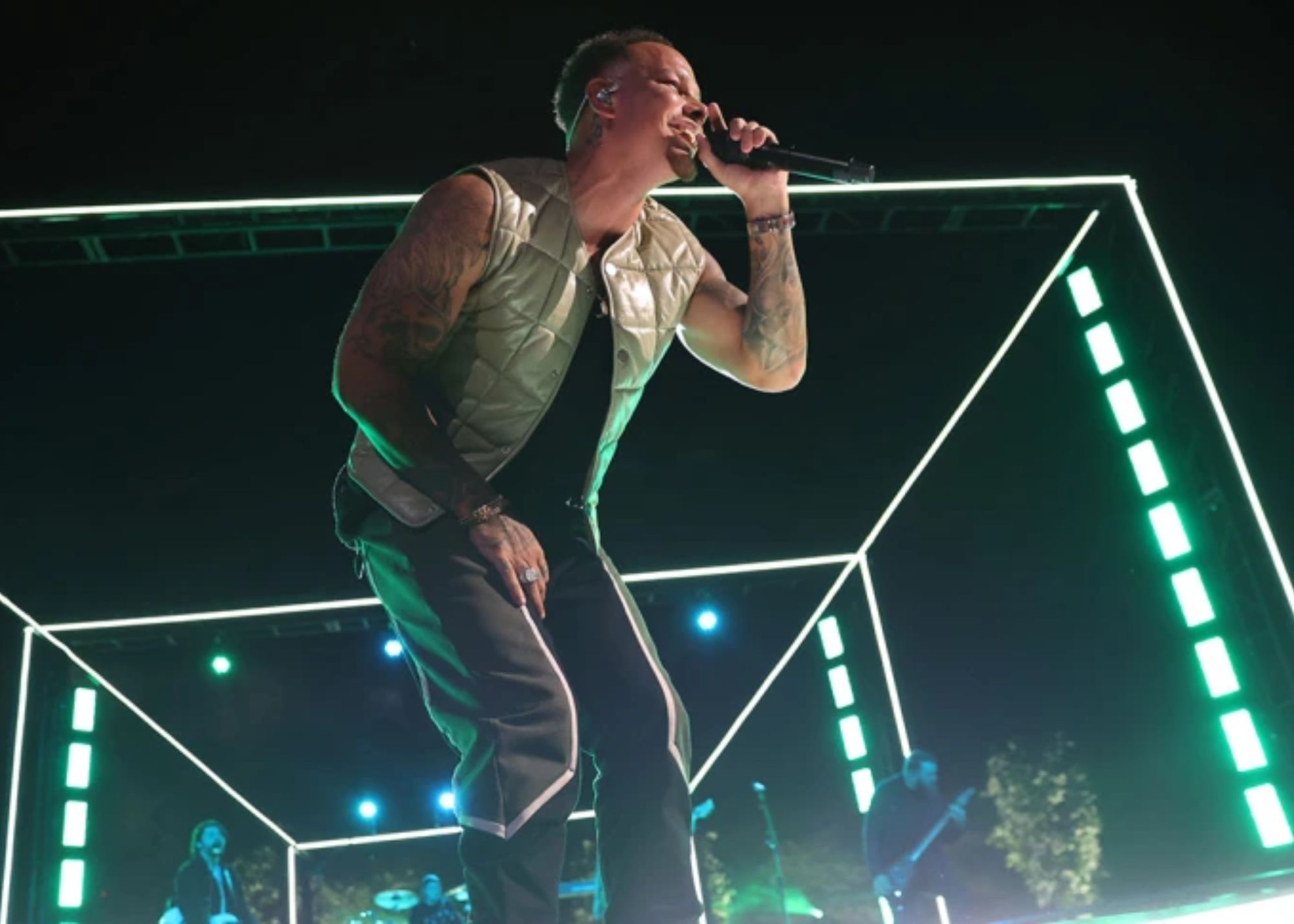 Kane Brown is performing on stage, surrounded by bright neon lights