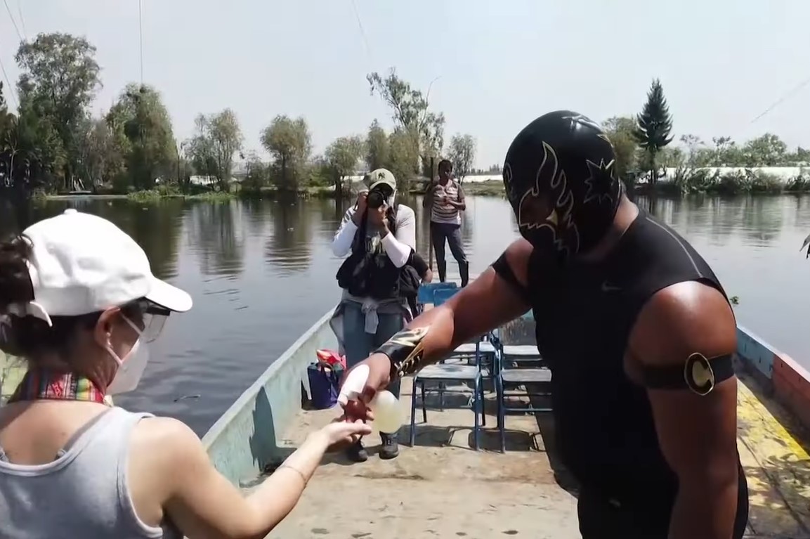 A masked male wrestler spraying the hand of a female boat passenger with a COVID-19 sanitizer spray