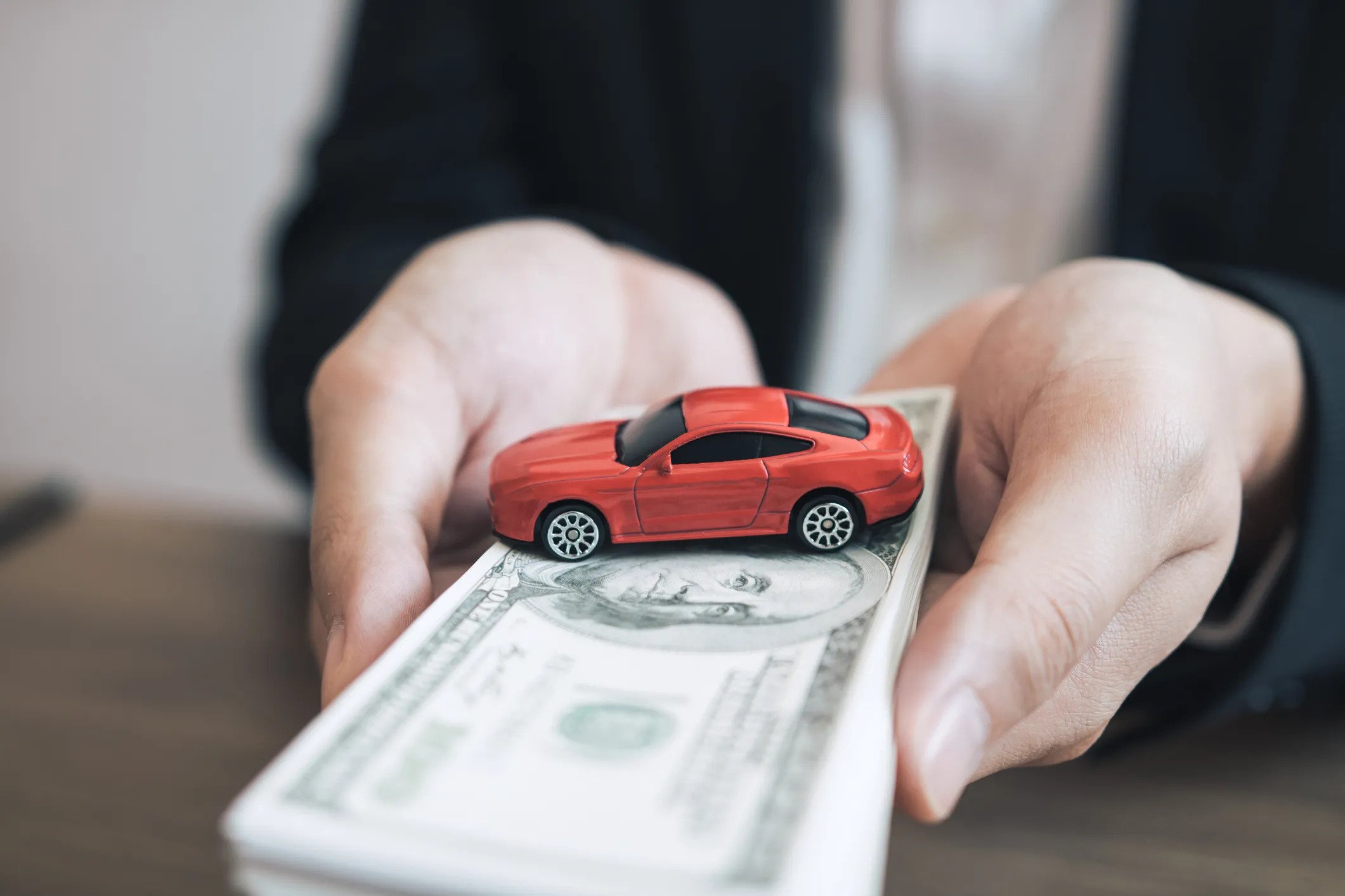 A lady holding a bundle of dollars and a red toy car