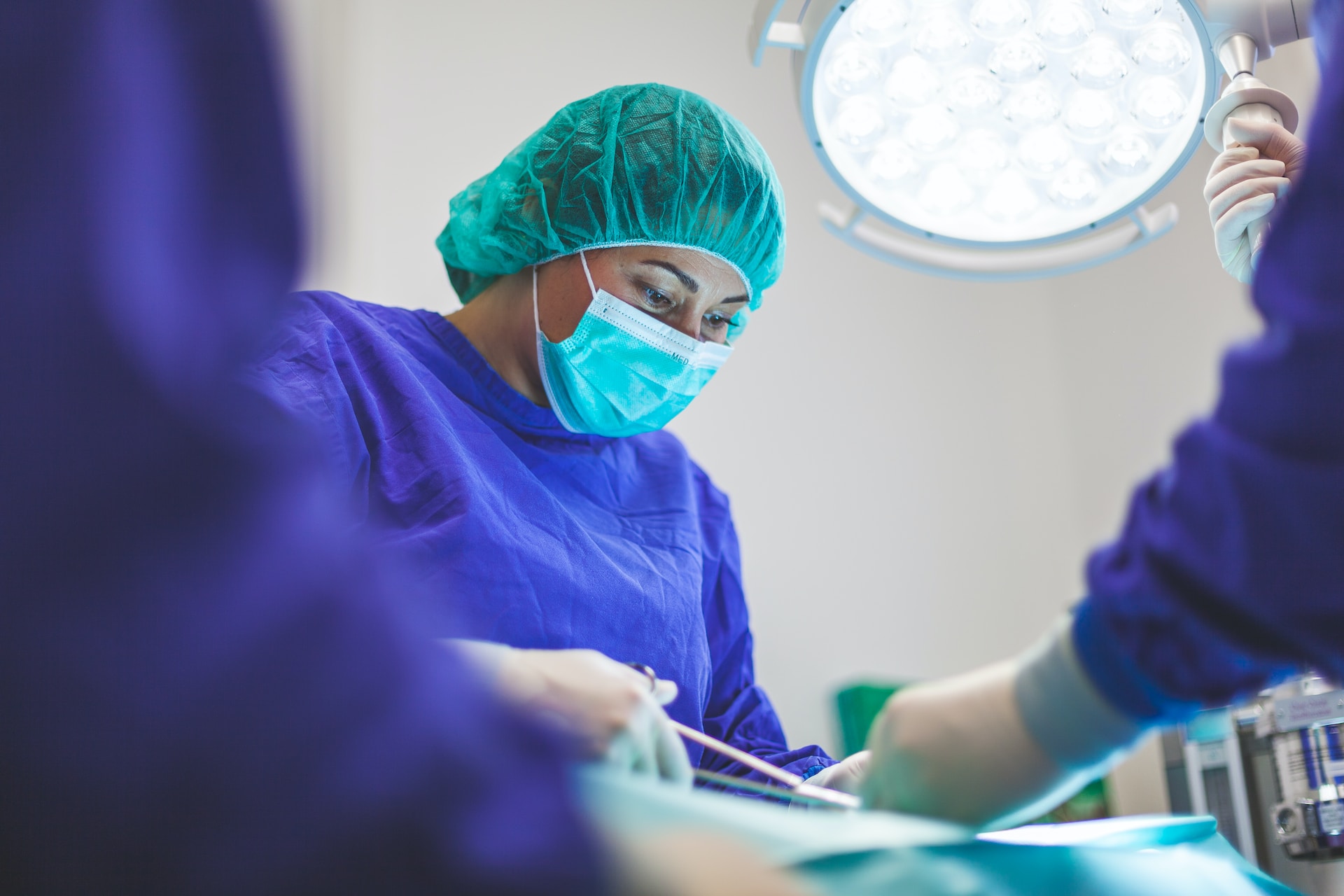 A female doctor in hairnet, face mask and blue scrubs holding forceps while doing an endometriosis surgery