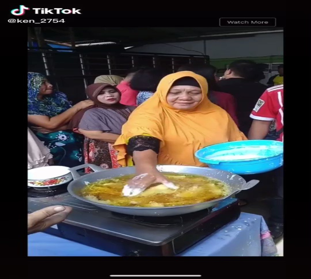 A lady wearing an orange scarf is frying something with her bare hands