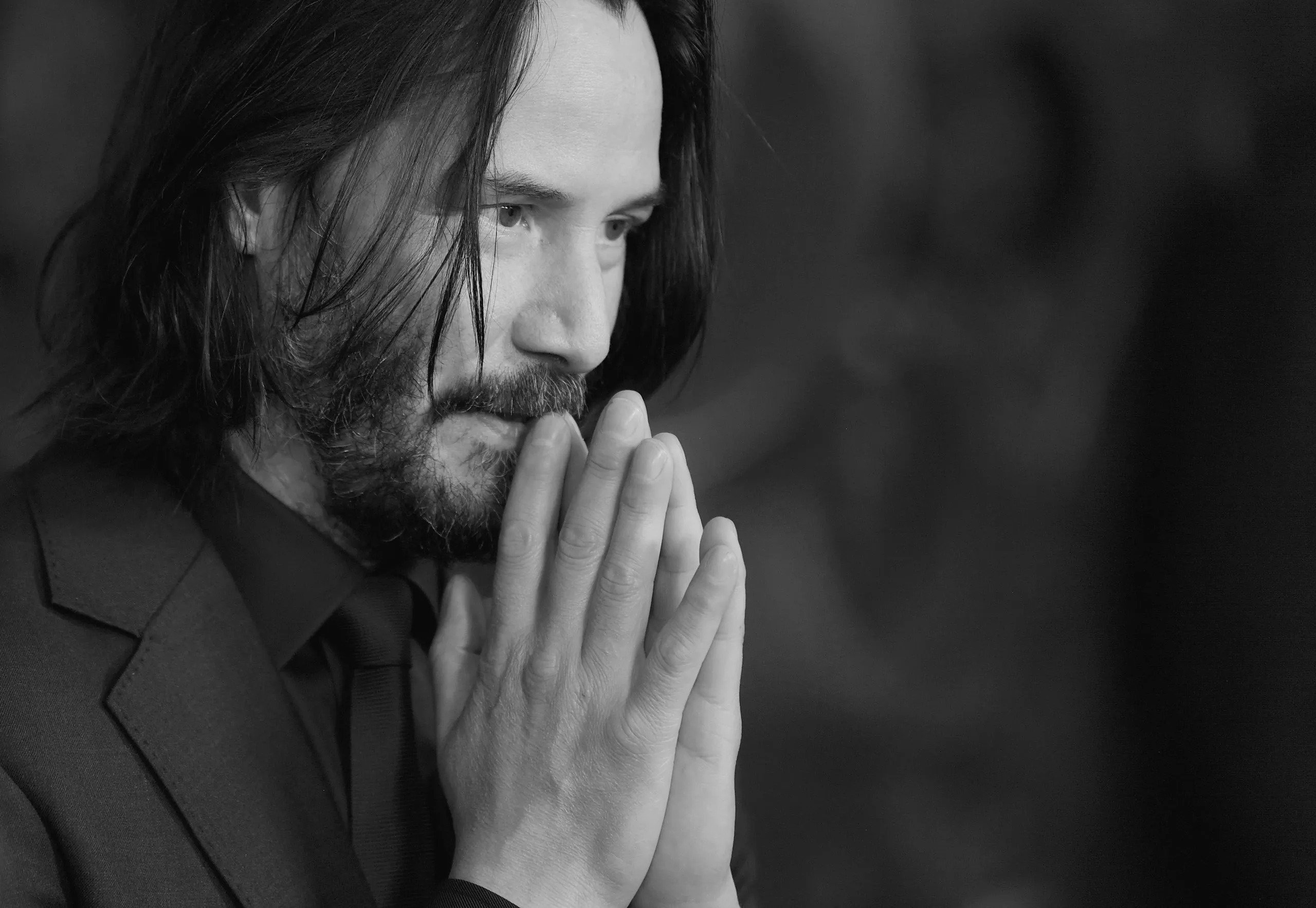 Keanu Reeves wearing a black suit and thinking about something