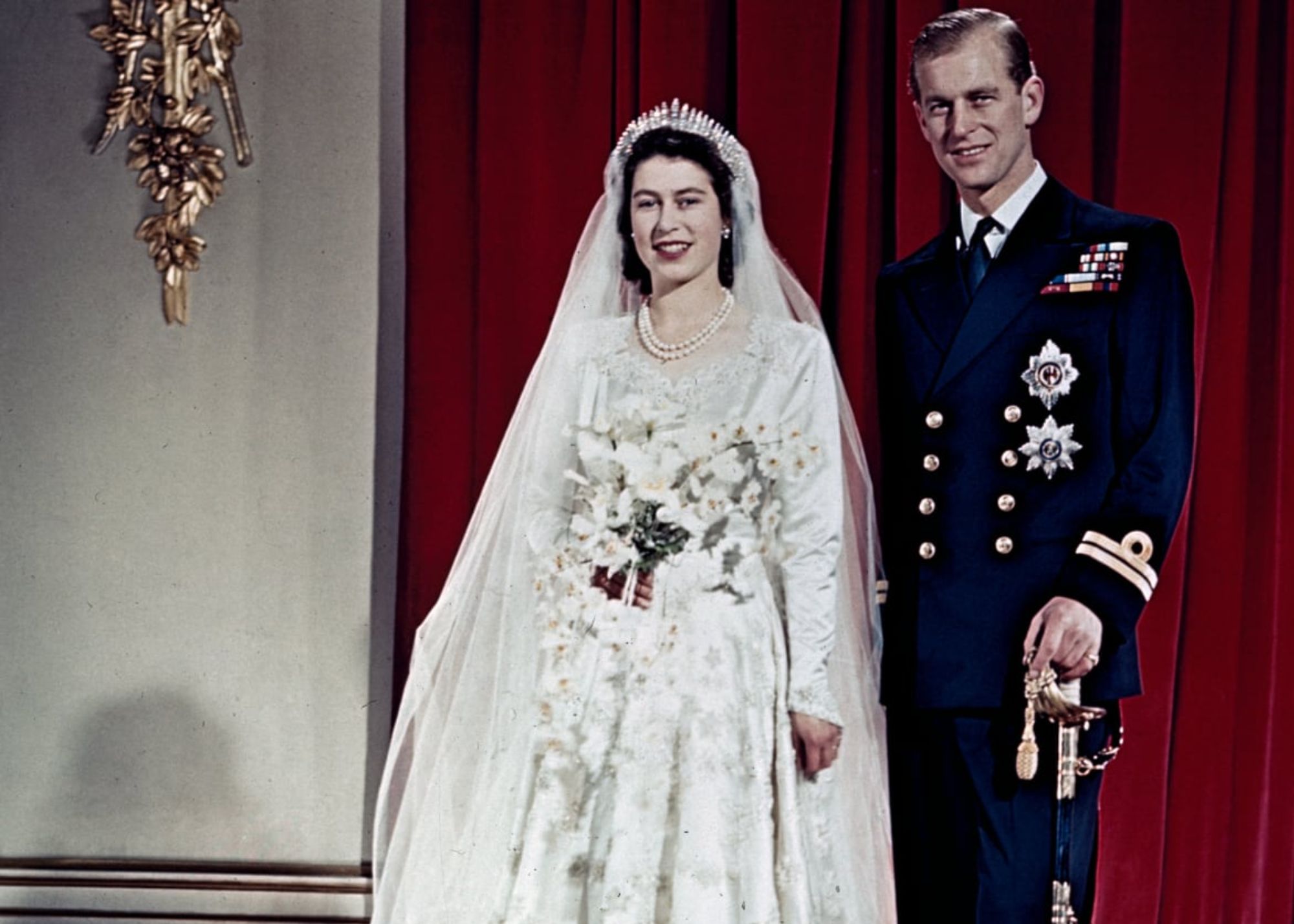 Queen Elizabeth II is wearing a white wedding dress, and Prince Philip is in full military uniform