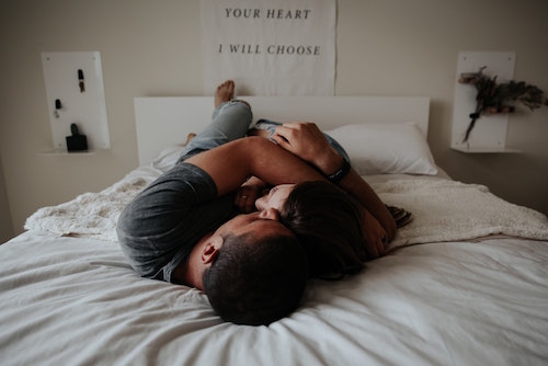 Man and woman lying on white bed hugging