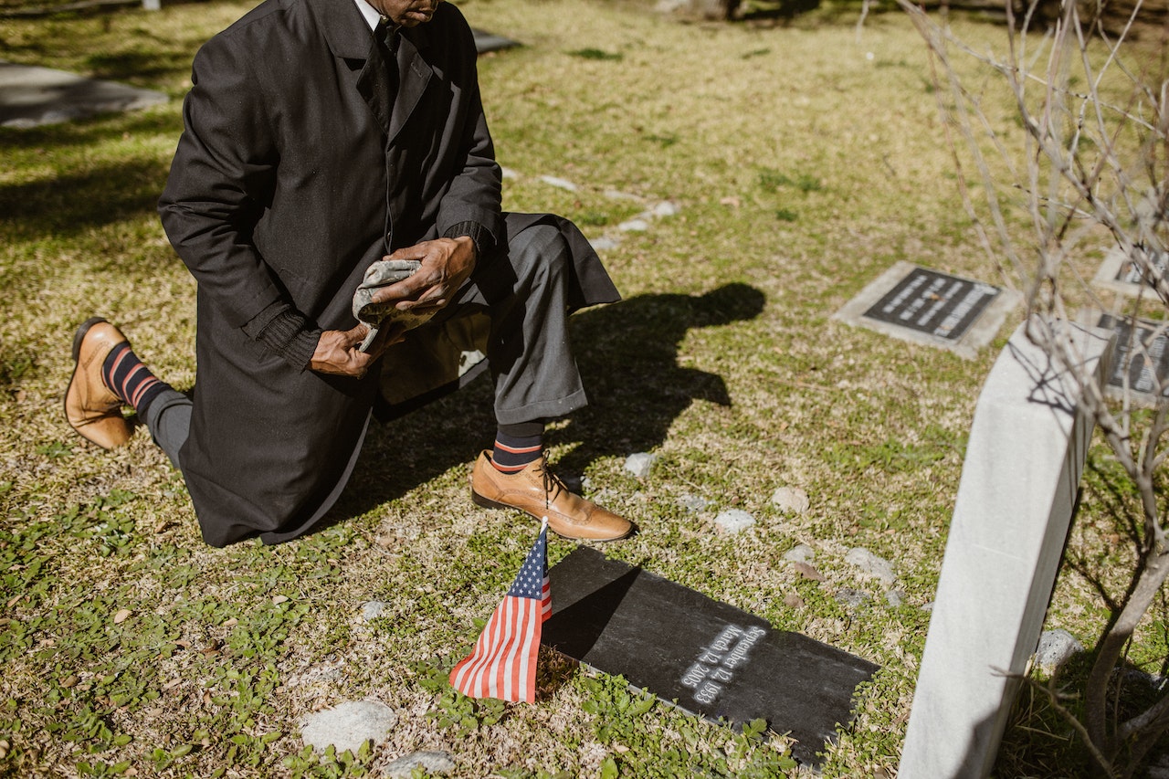 A Man Kneeling In Front of a Gravestone