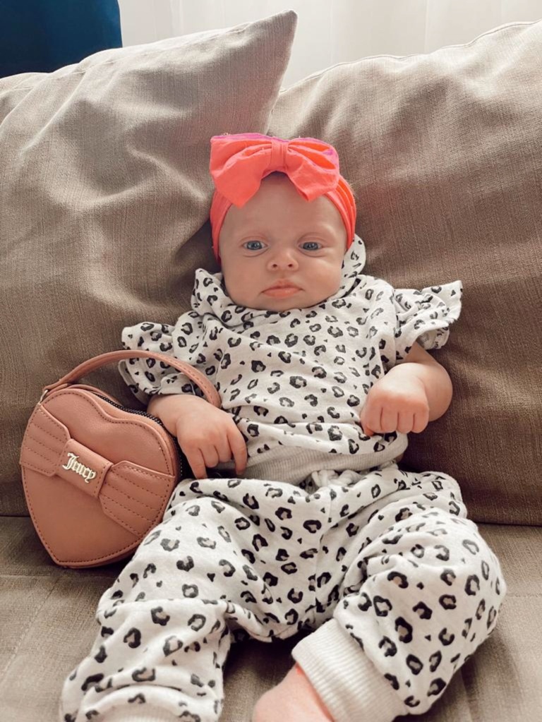 Baby girl wearing leopard printed pajama set, bright orange orange bow on her head and a heart shaped bag on hand