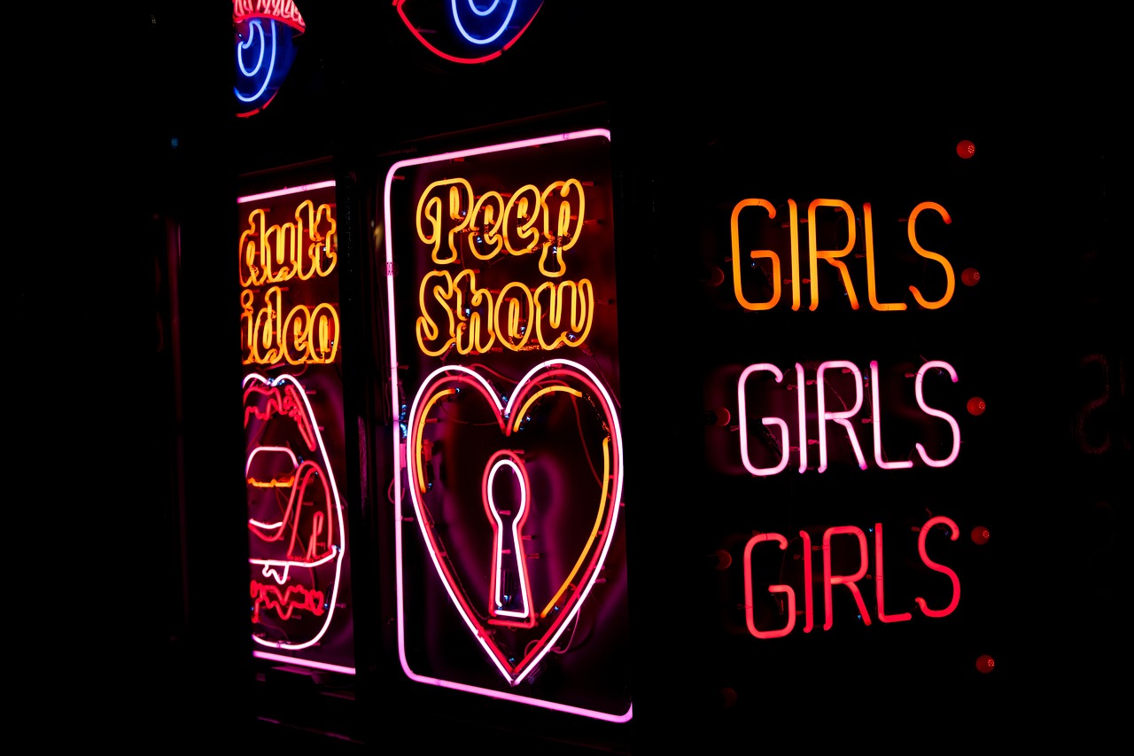 ‘peep show’ neon sign with an outline of a heart with a keyhole in the middle and three ‘girls’ neon signs