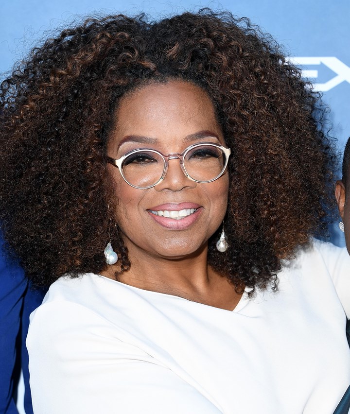 Oprah Winfrey wearing an eyeglass and huge earrings smiling