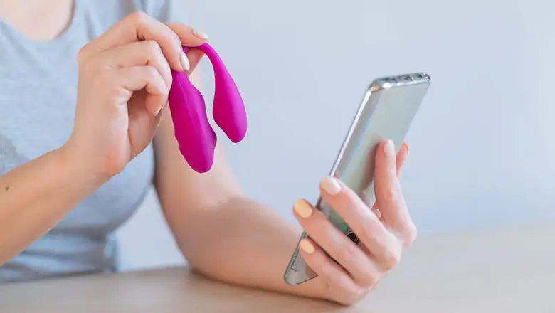 A woman holding a oink vibrator and a smartphone