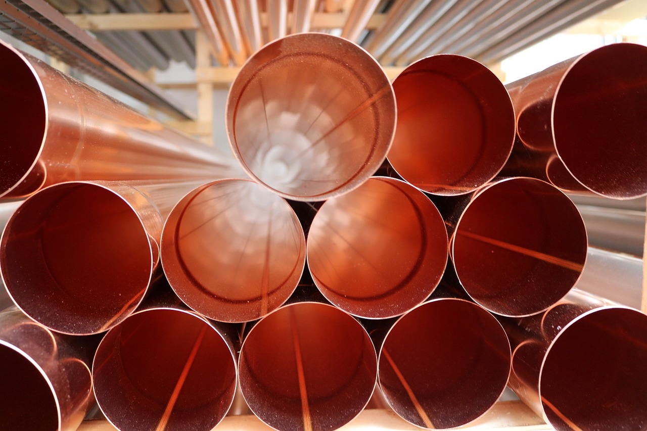 A pile of 13 circular copper tubes, with more circular tubes above them in the background