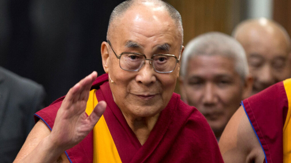 Dalai Lama wearing glasses with his arm raised