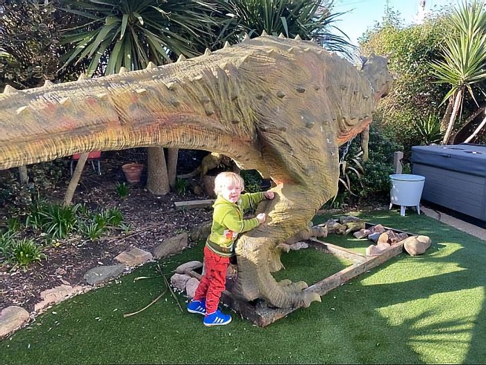 Happy kid leaning to his gigantic new dinosaur statue