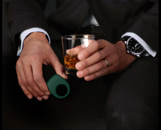 A man drinking whiskey holding a green vibrator ring