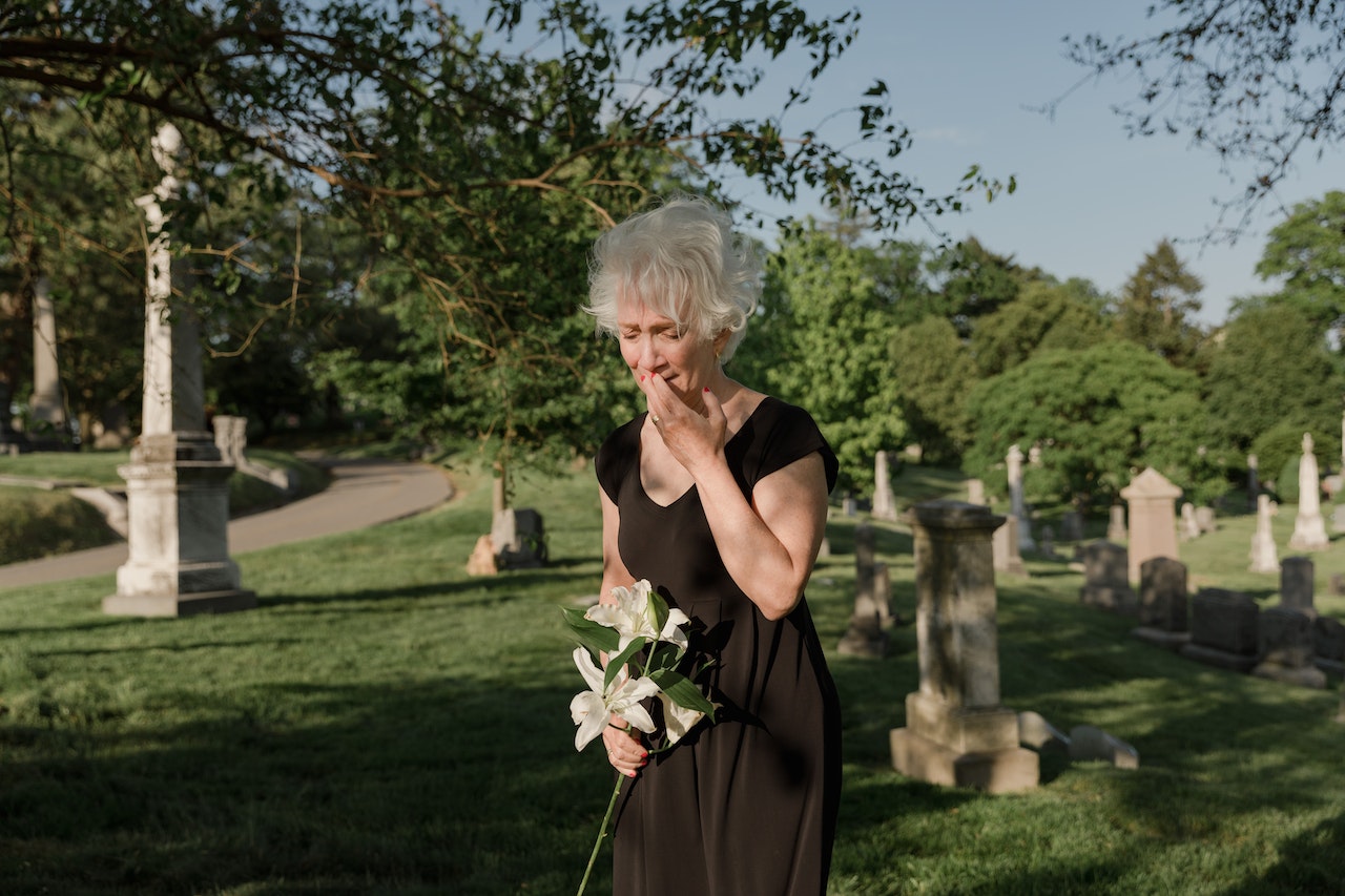 A Woman Holding a Stem of White Flowers while Crying on a Cemetery