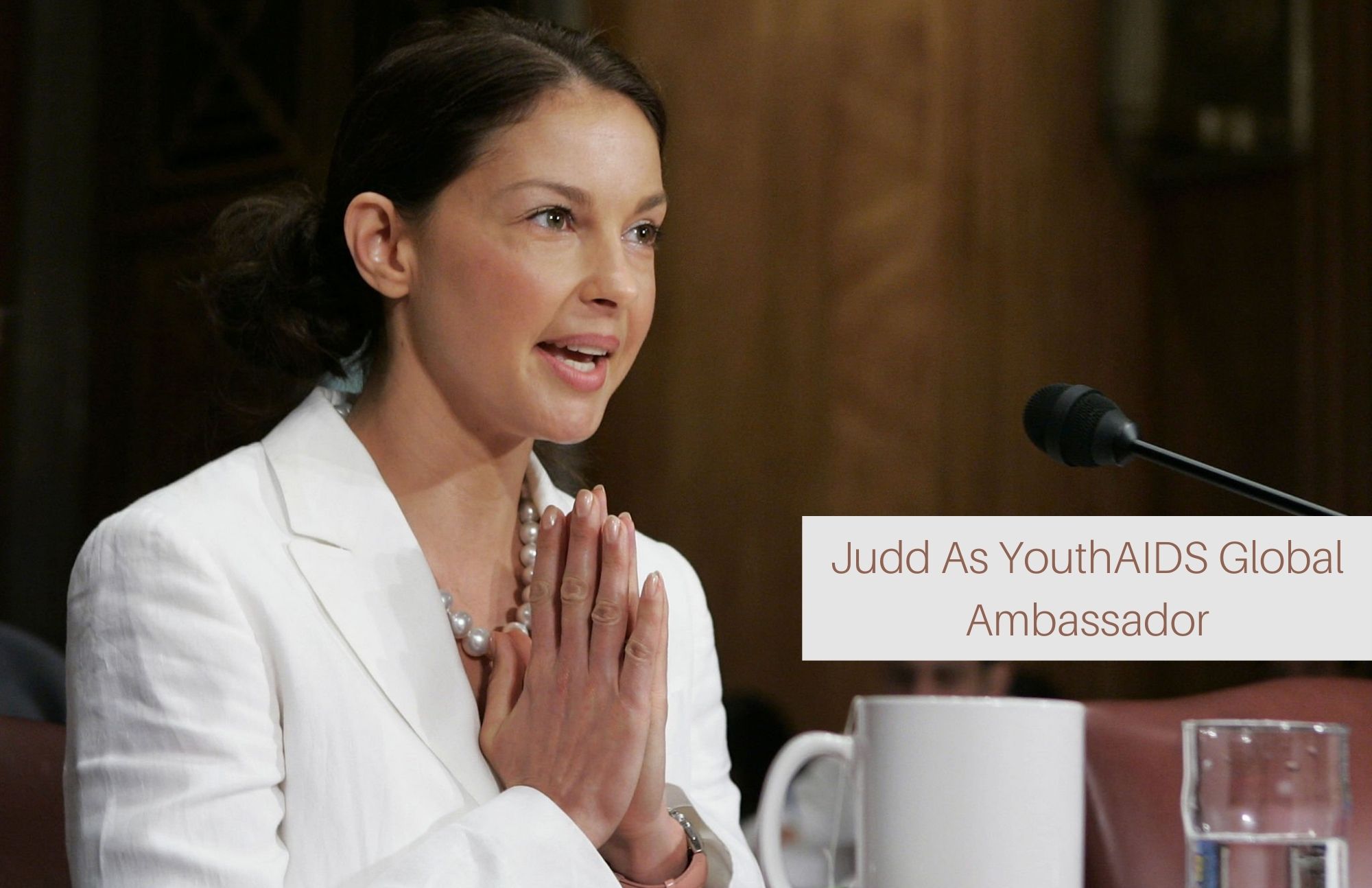 Ashley Judd is seen in a forum wearing a white dress with her hands clasped together