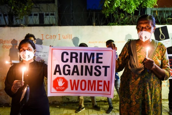 Two women holding candles and a banner stating "Crime Against Women"